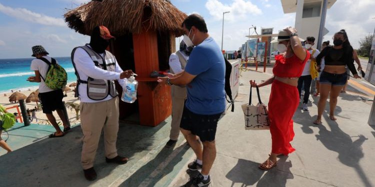 Un hombre reparte líquido desinfectante a turistas en la playa en Cancún, en enero.