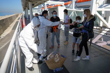 Los pasajeros Stefania Battistoni, de derecha a izquierda, sus hijos Dasteen y Samuel Pacifici y su madre Loredana Merlo dejan que saniticen sus equipajes de mano antes de abordar al crucero MSC Grandiosa en Civitavecchia, cerca de Roma, el 31 de marzo de 2021 (Foto AP/Andrew Medichini)