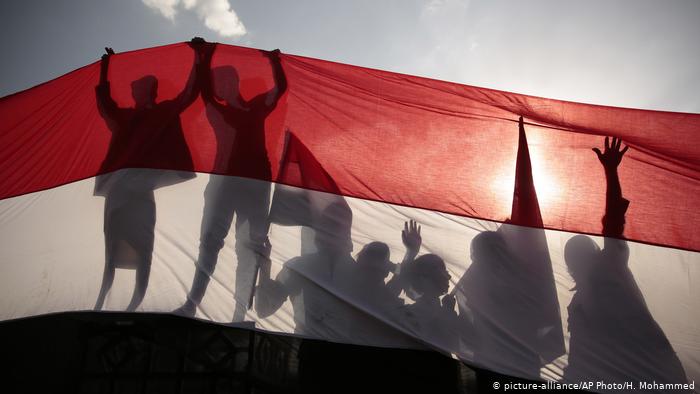 Yemeni men are silhouetted against a large representation of the Yemeni flag.