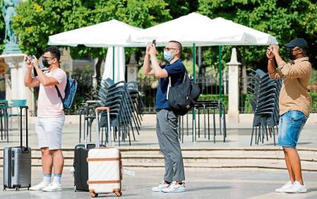 GRAFCVA5185. VALENCIA, 21/05/2021.- Tres turistas cargados con sus maletas realizan una foto en la plaza de la Virgen cuando el presidente del Gobierno, Pedro Sánchez, ha anunciado este viernes que a partir del 7 de junio todas las personas vacunadas, con independencia del país del que provengan, podrán entrar en España. EFE/Ana Escobar