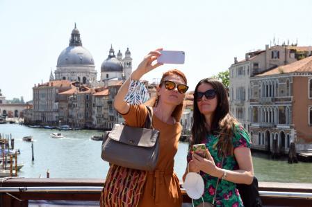 (FILES) In this file photo taken on June 03, 2021, tourists take selfie pictures on the Ponte dell'Accademia bridge over the grand canal in Venice. - Thousands have been separated from spouses, children or grandparents because of the tight lockdown of the country's frontiers, yet to be lifted despite the widespread distribution of vaccines on both sides of the Atlantic. Many are pressuring the administration of President Joe Biden to permit general travel to and from the US, with families spilling their anguish and anger over the forced separations onto social media. (Photo by ANDREA PATTARO / AFP)
