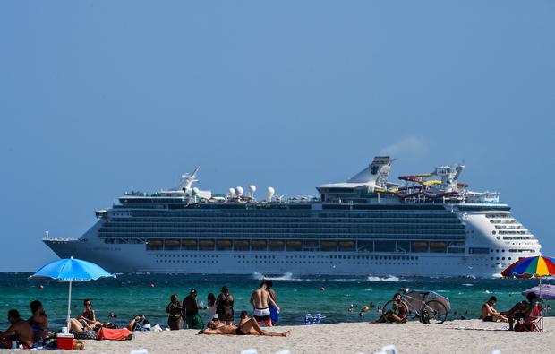 esta foto del 2 de julio del 2020 muestra a un crucero navegando mientras la gente se relaja en Miami Beach, Florida. (Foto: AFP)