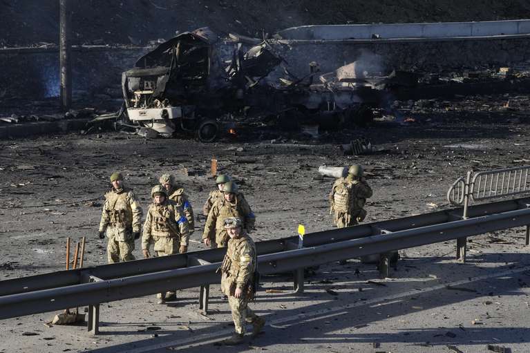 Soldados ucranianos caminan por delante de los restos de un camión militar calcinado en una calle de Kiev, Ucrania, el 26 de febrero de 2022. (AP Foto/Efrem Lukatsky)
