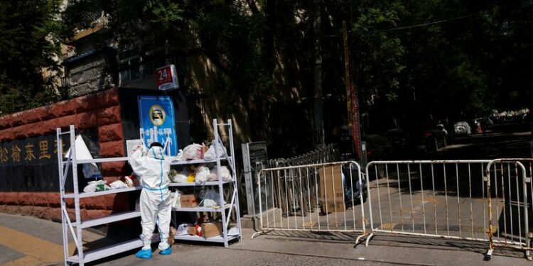 Una persona con traje de protección clasifica las entregas en un estante fuera de un área bajo confinamiento, durante la pandemia de COVID-19, en Pekín, China, 2 de mayo de 2022. REUTERS/Carlos García Rawlins