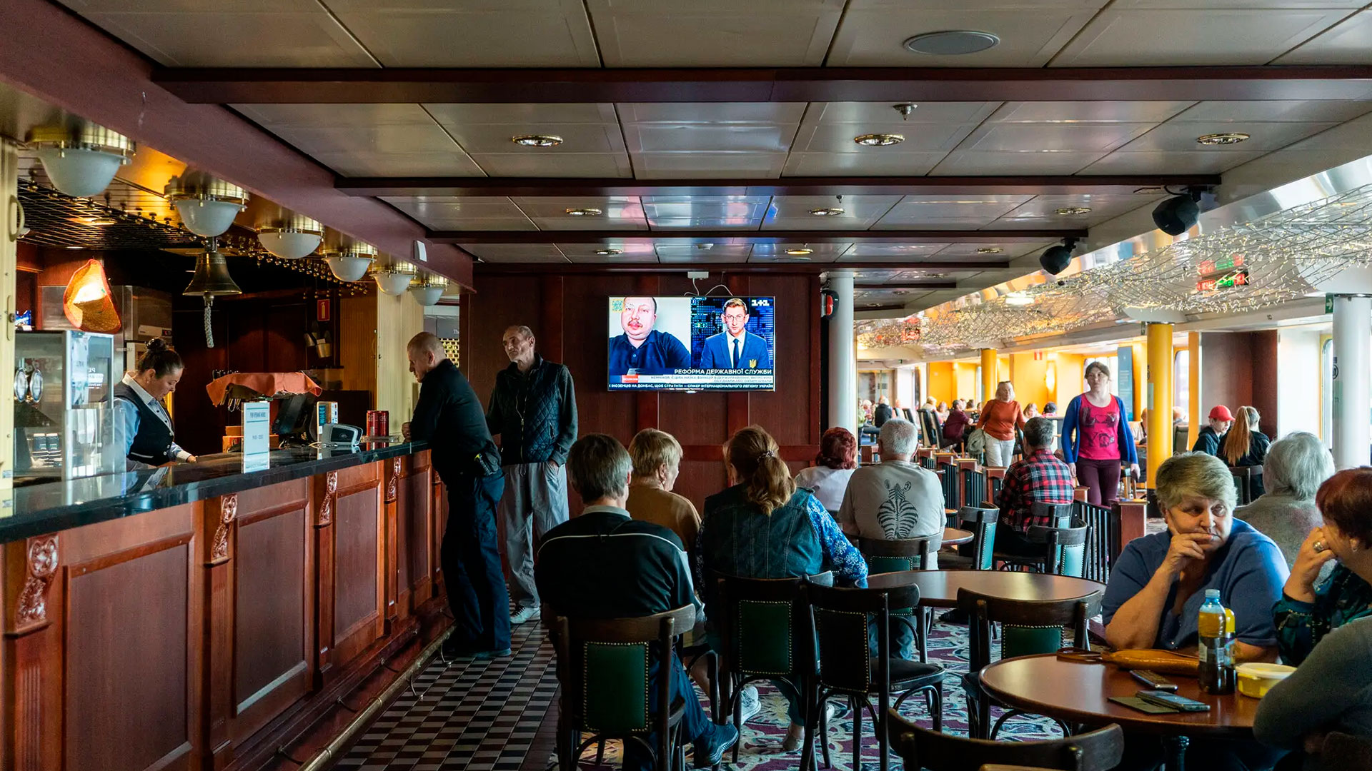 Los residentes del barco se reúnen en un salón para ver las noticias de Ucrania (Marta Giaccone para The New York Times)