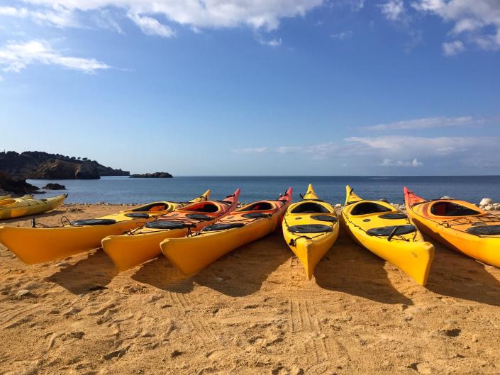 Fila de kayaks amarillos alineados en la playa con cielos azules en el fondo