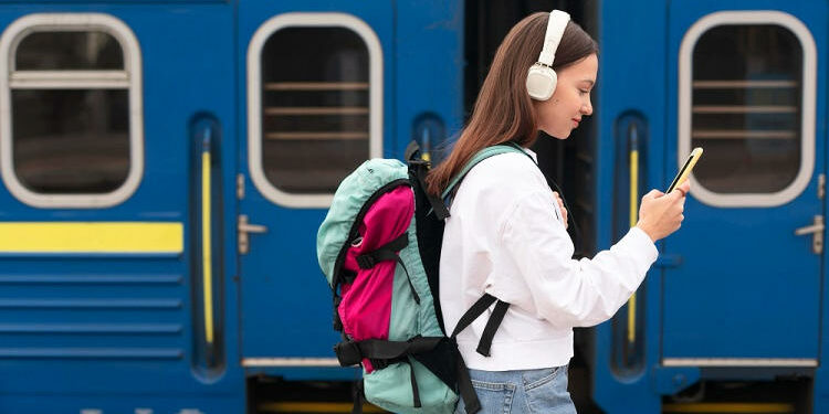 Joven con cascos y mochila esperando el tren.