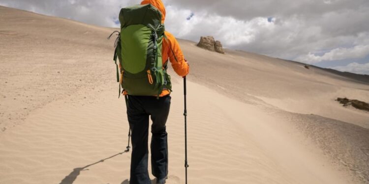 Chica caminando por duna de arena con su mochila de viaje