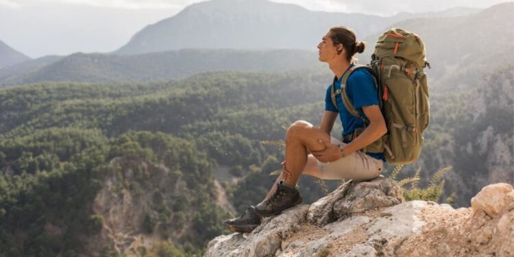 Mochilero sentado sobre una piedra con vista a zona natural