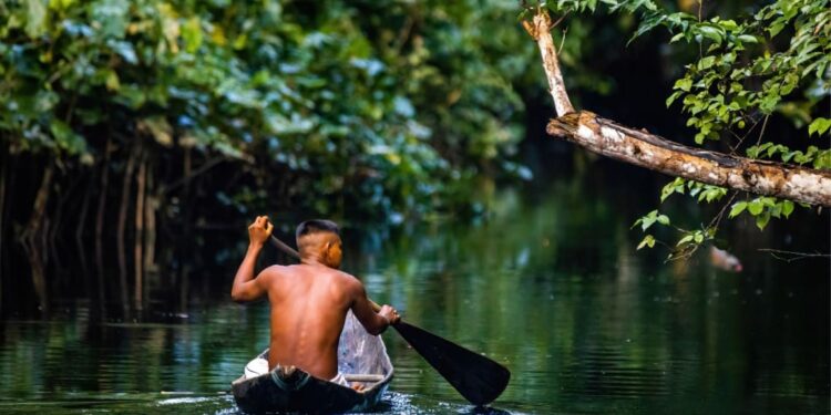 Joven en canoa remando por río del Amazonas