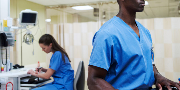 A photo shows a female and male nurse working at computers inside a hospital.