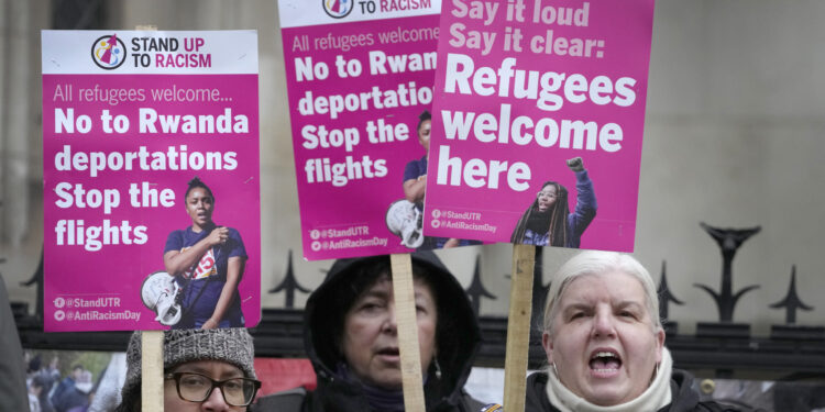 Activistas del grupo Stand Up To Racism sostienen carteles ante el Alto Tribunal de Londres el lunes 19 de diciembre de 2022. El controvertido plan del gobierno británico de enviar a solicitantes de asilo a Ruanda en un viaje sólo de ida es legal, según concluyeron el lunes los jueces del Alto Tribunal británico. (AP Foto/Kirsty Wigglesworth)