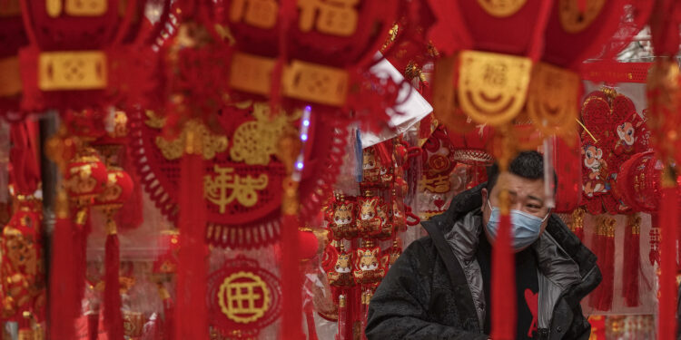 Un hombre, con mascarilla para protegerse del coronavirus, compra decoraciones para el Año Nuevo Lunar en un puesto en Beijing, el 7 de enero de 2023. (AP Foto/Andy Wong)