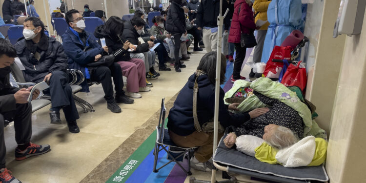 Una mujer cuida a un familiar mayor tendido en una camilla mientras recibe tratamiento intravenoso en una sala de emergencias atestada de un hospital de Beijing, el 5 de enero de 2023. (AP Foto/Andy Wong)
