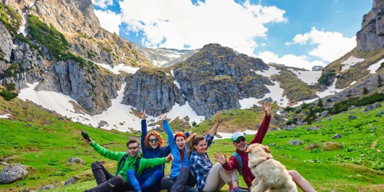 Grupo de jóvenes con perro levantando los brazos para foto en zona natural con montañas