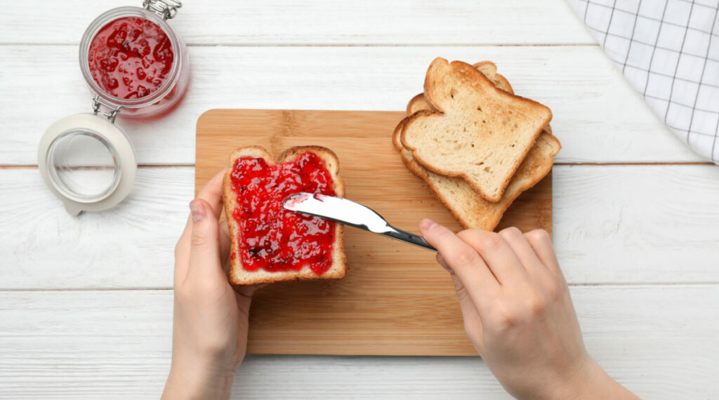 A person spreading jam onto a piece of bread
