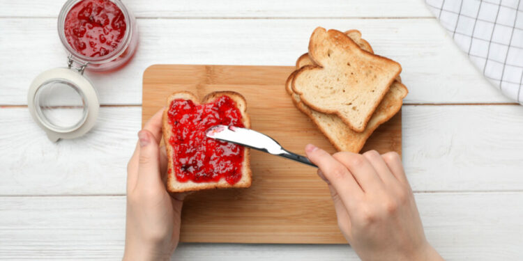 A person spreading jam onto a piece of bread