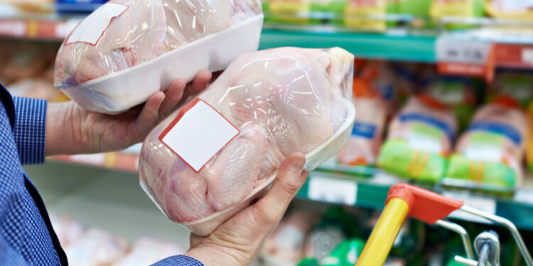 A shopper in a grocery store compares chicken meat, representing the poultry price-fixing settlement