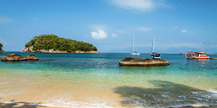 A beach on a sunny day with boats in the water in Ubatuba, Brazil.