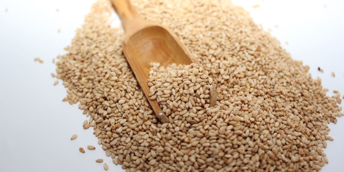 A photo of a wooden scoop laying in a pile of sesame seeds.