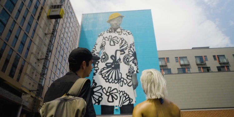 Two people gaze up at the untitled Amy Sherald mural in Philadelphia during the 1st Look program