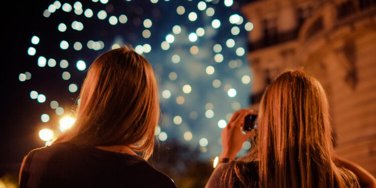 Dos mujeres de espalda ven juegos artificiales en un cielo oscuro