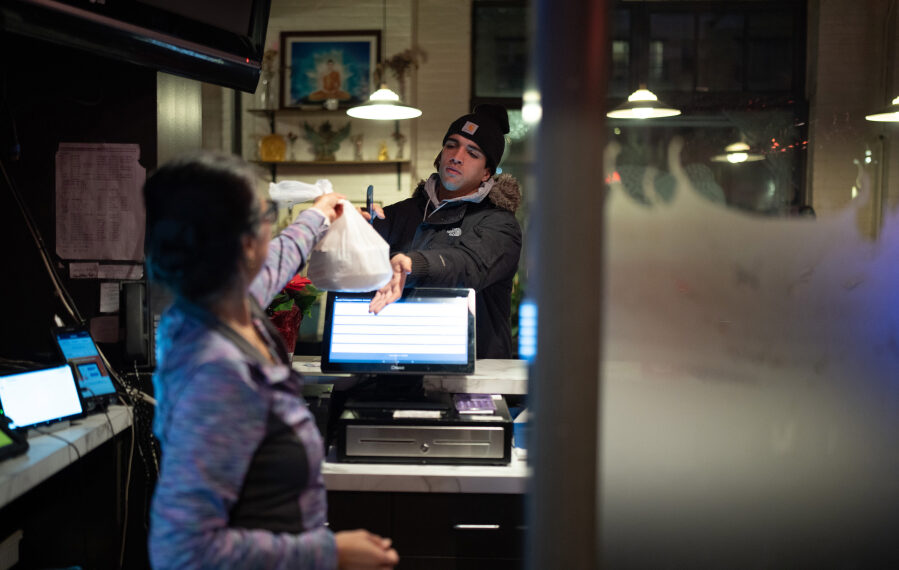 Sam Simonson hands a takeout order to a DoorDash delivery person at Sawatdee in Minneapolis on Thursday night, Dec. 14, 2023. Third party delivery food delivery services are a growing share of business at fast food restaurants and for other restaurants with cuisines that travel well, like the Thai menu at Sawatdee in Minneapolis, where they account for 30% of their business.