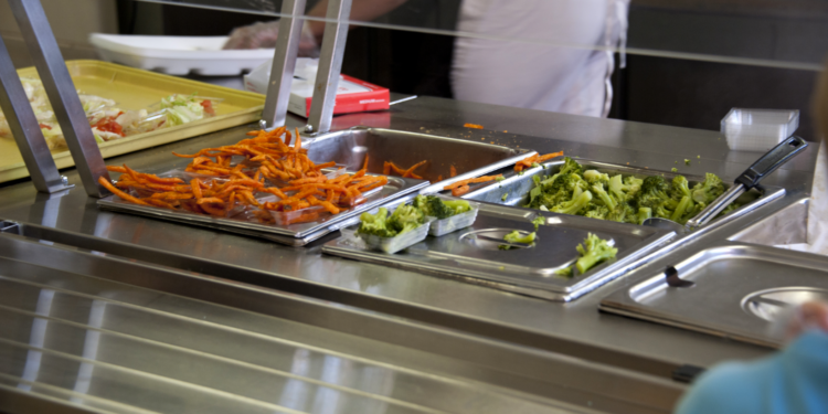 Trays of vegetables are placed along the serving line of a school cafeteria
