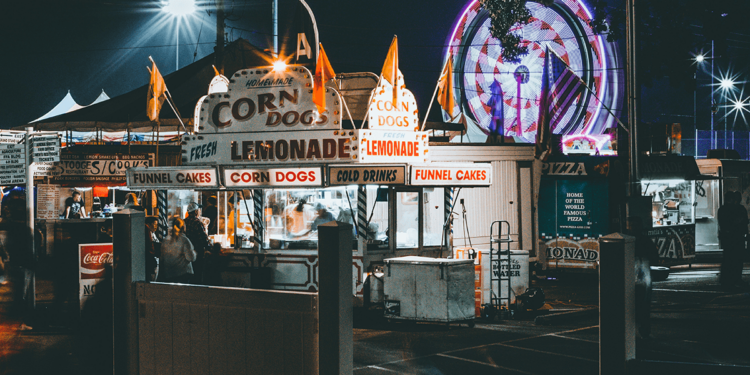 A brightly-lit corn dog stand at a carnival at night.