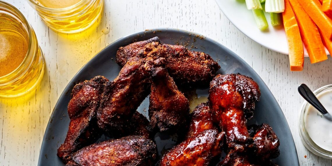 Plate of wings next to plates of carrots and celery and beer.