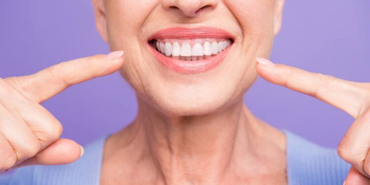 foods for healthy gums: Concept of having strong healthy straight white perfect teeth at old age. Cropped portrait of beaming smile female pensioner pointing on her teeth, isolated over violet background