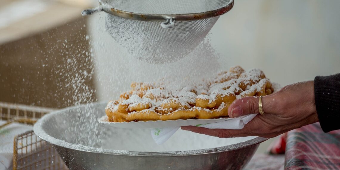 A funnel cake being sprinkled with powdered sugar.