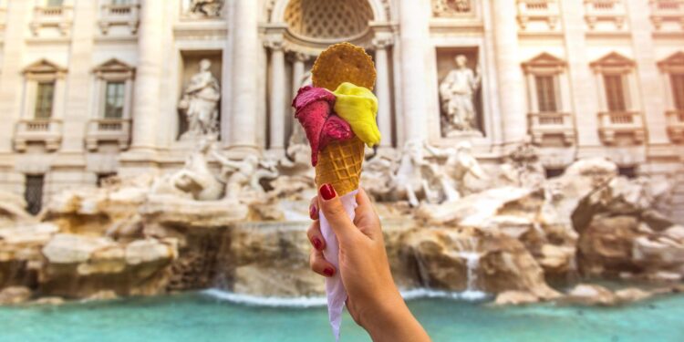 Una mano sostiene un helado frente a la Fontana di Trevi de Roma.