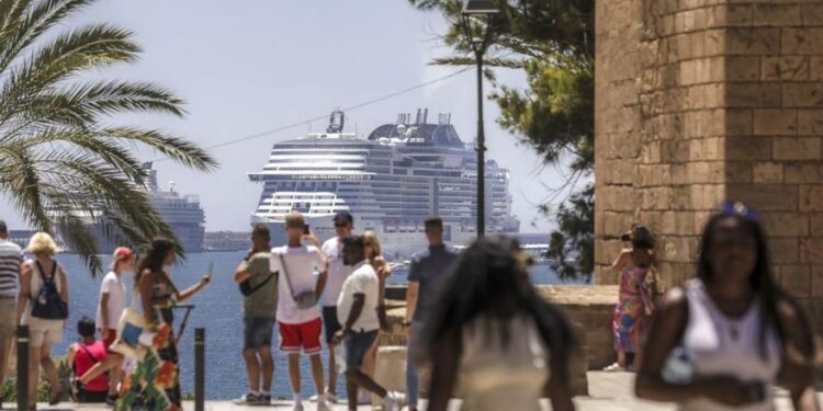 Varios turistas frente a la Seu con uno de los cruceros que atracan en Palma.