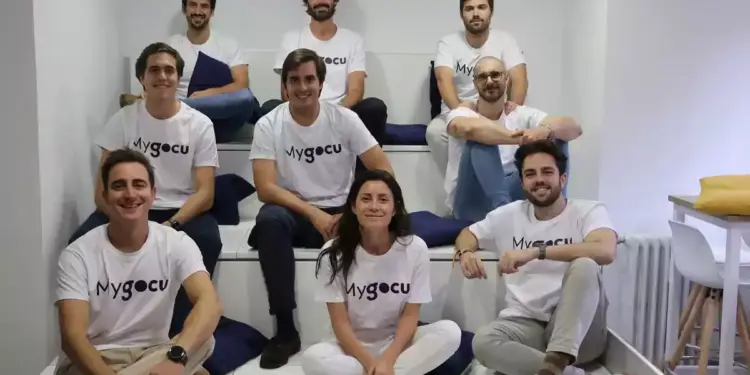 Un grupo de personas sentadas en una estructura escalonada, todas vistiendo camisetas blancas con el logo de "Mygocu".