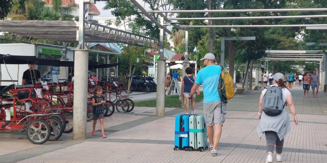 Turistas con maletas pasan junto a un tenderete de alquiler de bicicletas en Santa Susanna.