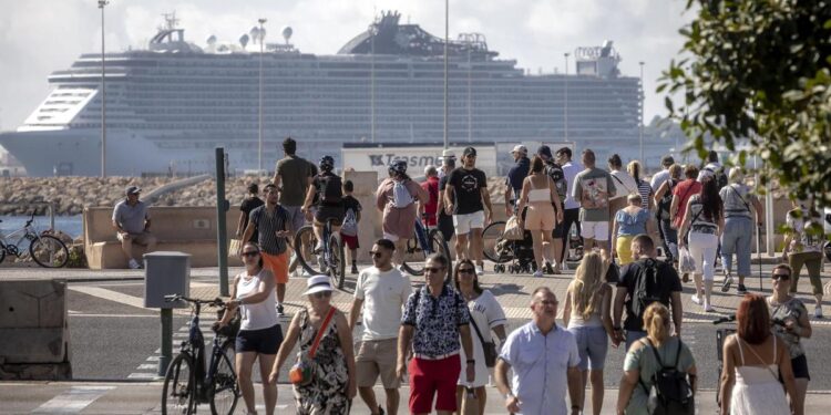 Turistas en el centro de Palma con un crucero de grandes dimensiones al fondo.