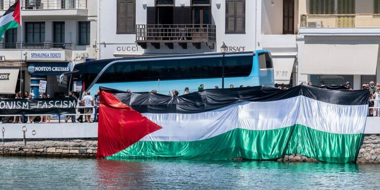 Manifestantes propalestinos se reúnen durante la llegada de un barco que transporta turistas israelíes, al fondo, en el puerto de Agios Nikolaos, en la isla de Creta, Grecia.