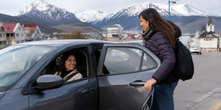 Mujer sube a un auto con conductora en una calle con montañas nevadas de fondo