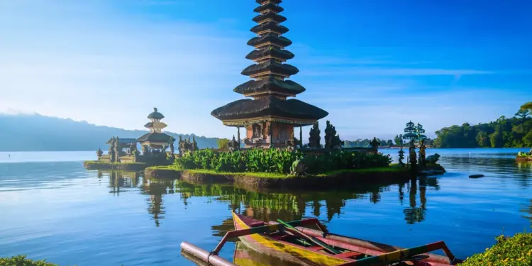 Paisaje de templo tradicional balinés sobre un lago con un pequeño bote en primer plano y reflejo del templo en el agua.