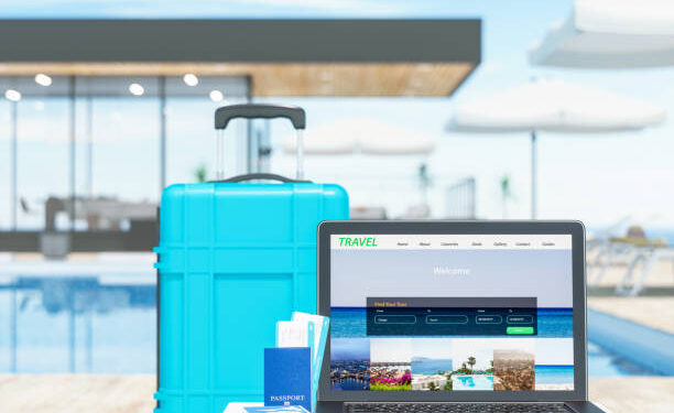 Laptop mostrando sitio web de viajes junto a maleta y pasaporte