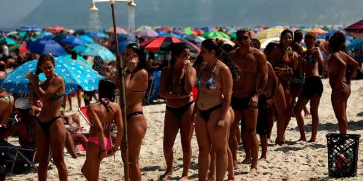 Bañistas hacen fila para refrescarse sin mantener la distancia social hoy, en la playa de Ipanema (EFE)